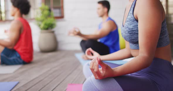 Midsection of biracial woman practicing yoga with group of diverse friends in backyard