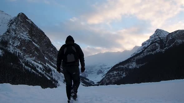 Man walking on frozen lake with mountains in background