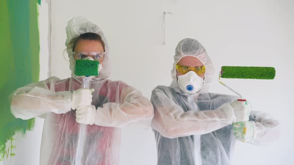 Couple in Protective Suits Poses with Paint Rollers in Room