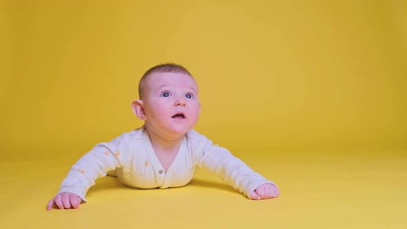 Infant baby boy looks in surprise while lying on his tummy, studio yellow background