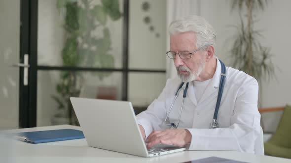 Senior Old Doctor Working on Laptop in Clinic
