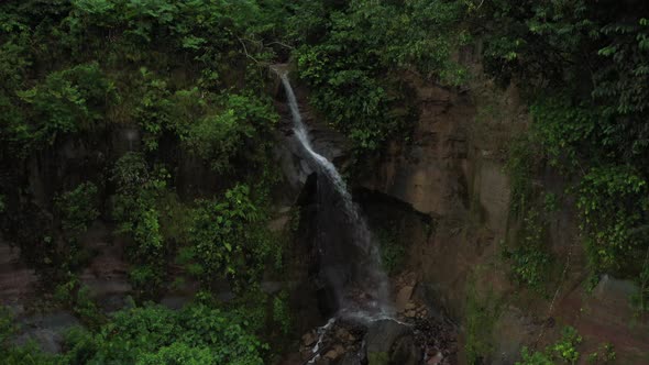 Aerial view starting in front of a waterfall and zooming out to top view of waterfall and rainforest