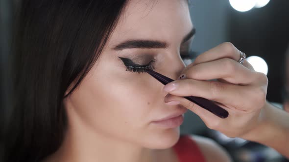 Closeup Makeup Artist Sticks False Eyelashes of a Beautiful Young Female Mode