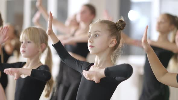 Confident Slim Girl Moving Up and Down in Fourth Ballet Position in Dancing School with Friends