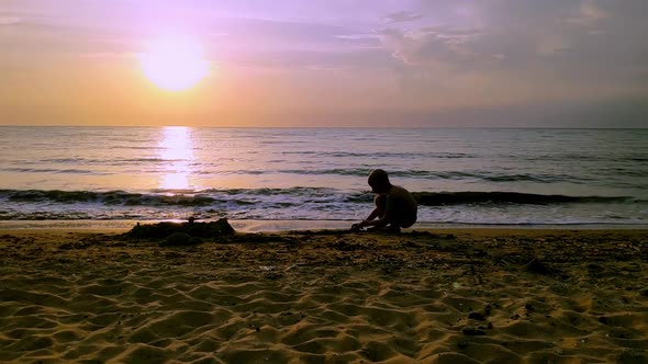 Boy at Sunset Playing on the Seashore Sitting on the Sand