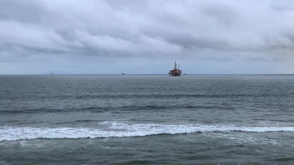 4k 60p, Offshore oil rig at dusk with a cloudy sky and waves rolling in.