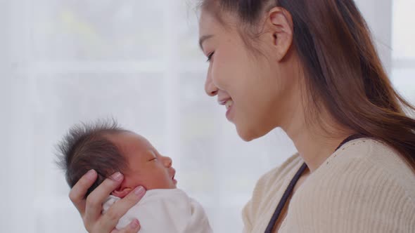 Asian mom holding baby newborn in hand and kissing on baby head sweet lovely