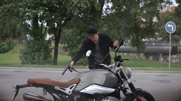 Young Man Washing His Scrambler Motorbike with Water Hose on the Street