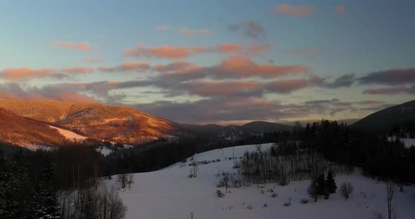 Aerial View of Mountains and Forest Covered with Snow at Sunset in Winter