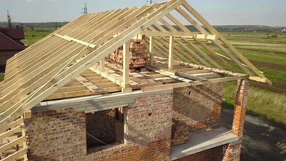 Aerial view of unfinished brick house with wooden roof frame structure under construction