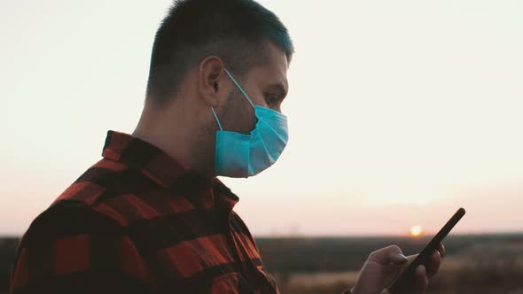 Handsome Young Man with a Medical Face Mask Use Smartphone on at Sunset Time