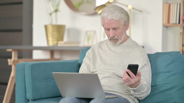 Old Man Working on Smartphone and Laptop on Sofa