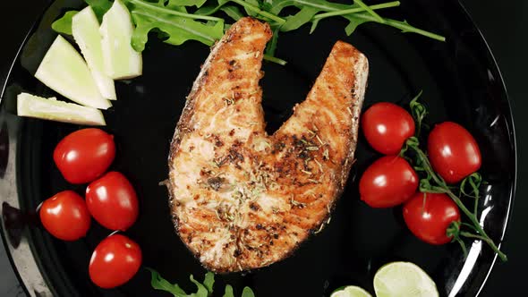 A Cooked Salmon Steak with the Addition of Aromatic Spices and Vegetables on a Black Serving Plate