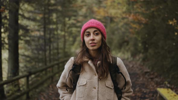 Smiling Hiker Woman in Pink Beanie Hiking in Forest in Autumn
