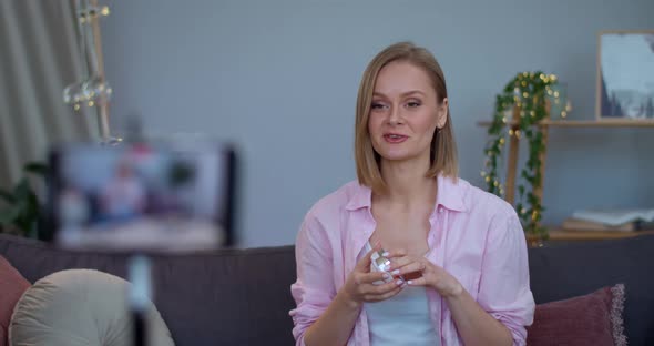 Young Beautiful Woman Talking and Looking in Compact Powder Case While Sitting on Sofa .Attractive