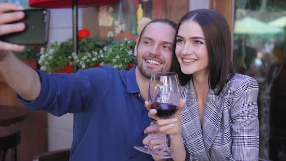 Happy Couple With Wine Taking Photos On Phone At Restaurant