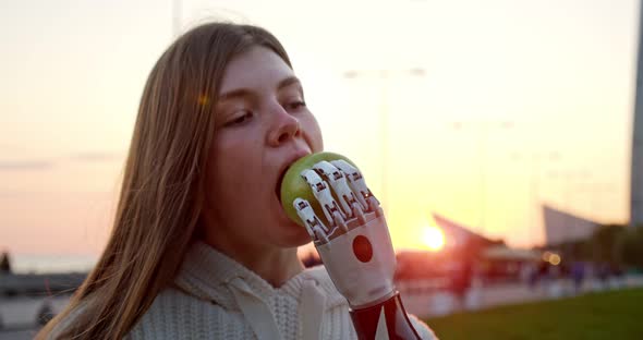 a Young Disabled Woman with a Bionic Arm Eats an Apple at Sunset