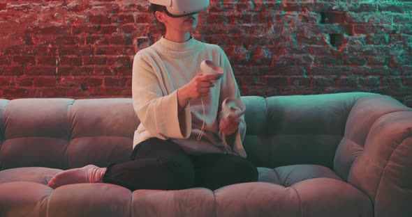 Young woman siting on the couch wearing vr goggles and husing handles to experience vr