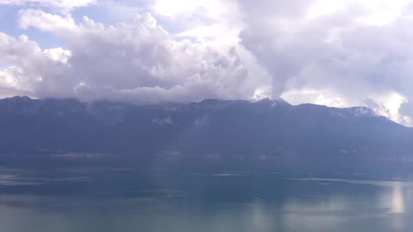 Aerial hyper lapse of clouds rolling over mountains near lake