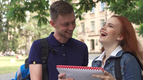 Female Student Asks Her Classmate About Something in Notebook on Campus