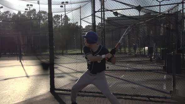 A young man practicing baseball at the batting cages.