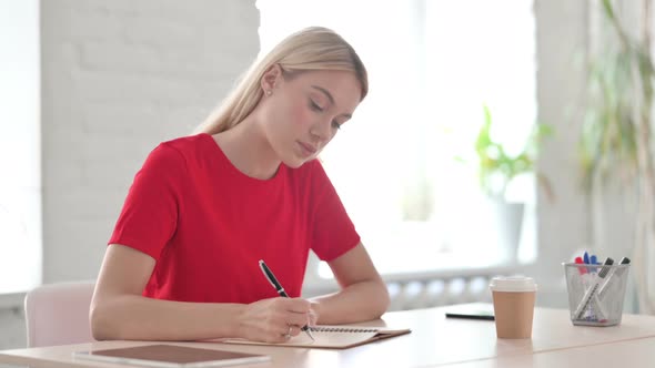 Young Blonde Woman Writing while Sitting in Office