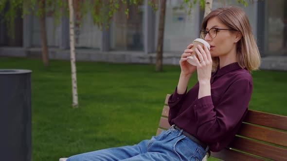 Close up business woman sitting on a bench while sipping coffee to-go.