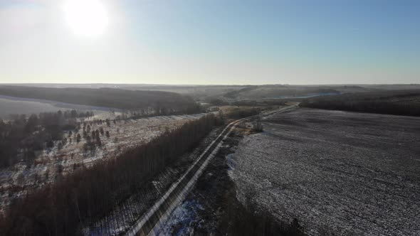 Flying over the road among the fields and woods towards the low sun