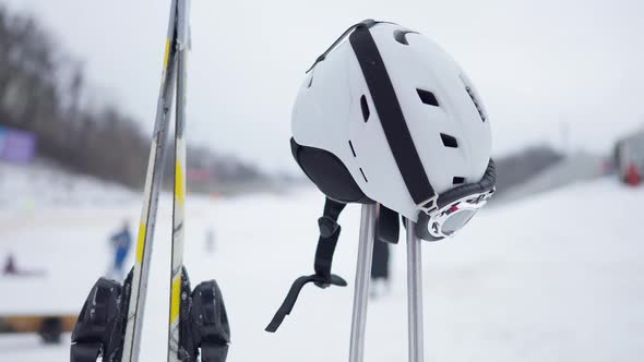 Ski Helmet on Poles with Skis and Blurred Winter Resort at Background