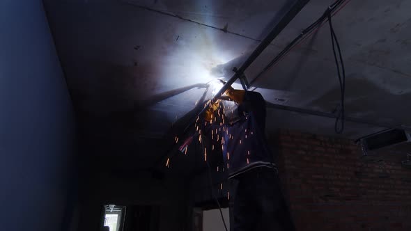 A Welder on a Construction Site Welds an Iron Pipe Under the Ceiling of the Room. The Welder Works