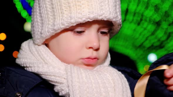 A Boy Stands Under Garlands on Christmas Day and Holds a Box of Gifts