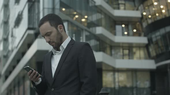 Young Businessman Reads a Text Message Standing Outside the Office