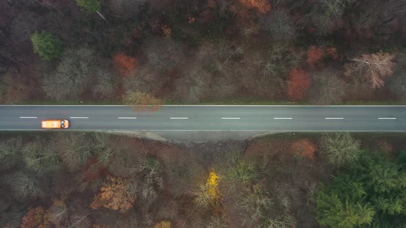 Orange transporter drives along a straight road, steady top down shot.