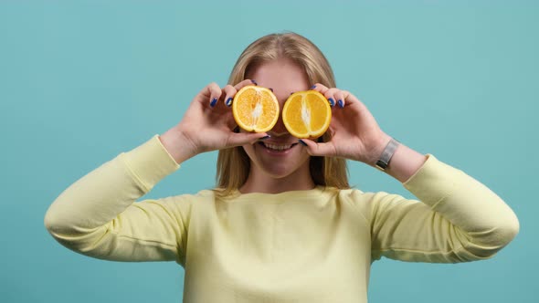 Funny Cheerful Girl Holding Two Halves of Orange Agains Her Eyes.