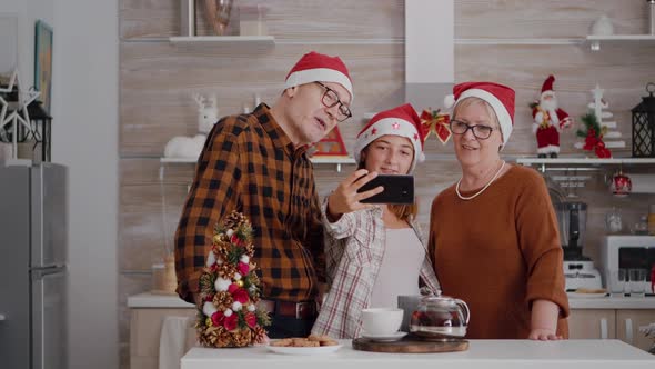 Happy Grandparents Standing at Table in Xmas Decorated Kitchen Taking Selfie Using Smartpgone