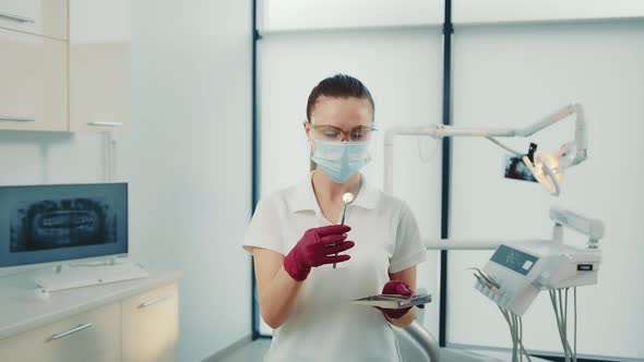 Female Dentist in Protective Mask Taking Intraoral Mirror From Tray in Medical Clinic