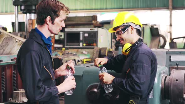 Tired Factory Workers Taking a Break and Talking to Coworker in the Factory