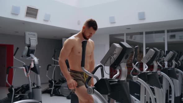 The Man Warms Up His Muscles on the Elliptical Bike in the Gym