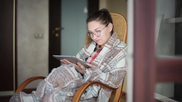 girl in a rocking chair with a tablet reads an e-book, news, or surfs Internet