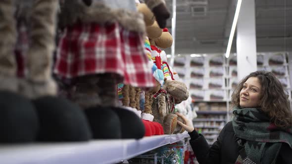 Young Curlyhaired Woman Chooses Christmas Presents in Mall