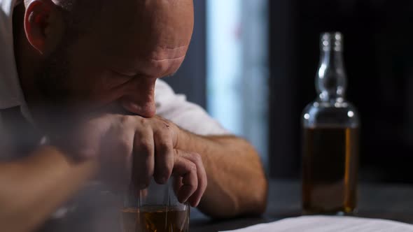 Pensive Man Leaning Hands on Glass of Whiskey