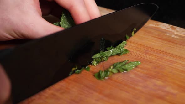 Cutting Peppermint leaves in slow motion with a black knife on chopping board.