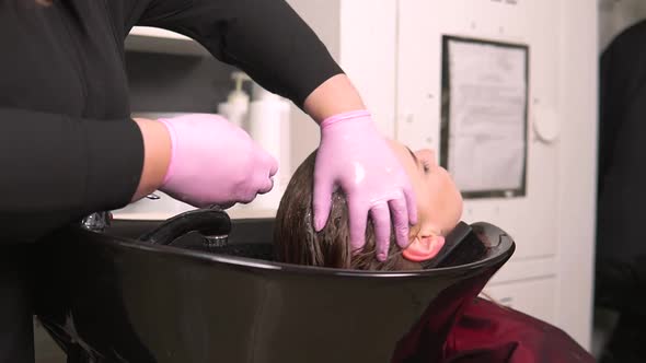 The Hairdresser Slowly Applies Shampoo to the Wet Hair of a Young Blonde Woman