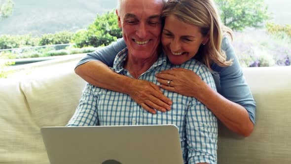 Smiling senior woman embracing a man in living room while using laptop