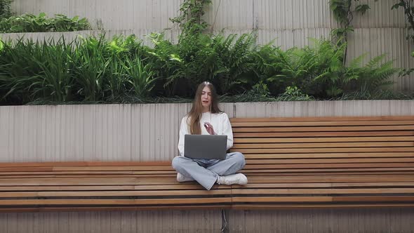 Young Female in Garden Using Laptop Communicates on Internet with Customer