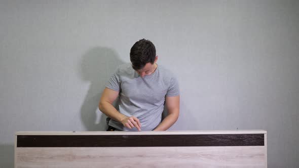 Man in a Gray Tshirt Assembles Furniture Using a Screwdriver