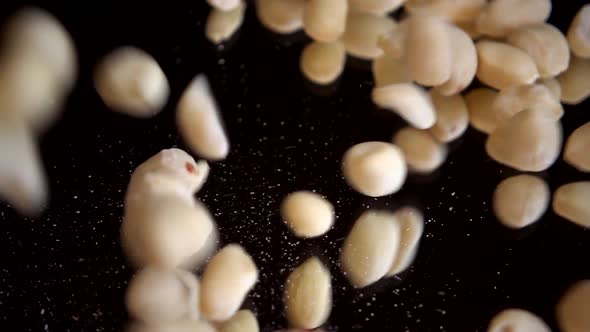 Raw blanched peanuts fall on a black mirror surface