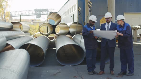  Manufacturing Engineer and Workers Looking at Blueprints at Plant