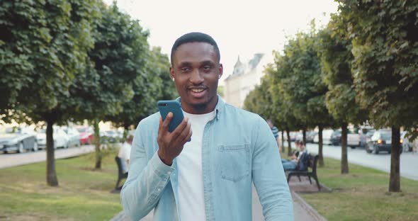 African American Walking on the Urban Alley with Green Trees and Enjoying Video Call