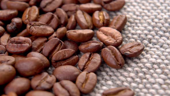 Roasted coffee beans on rough rustic jute cloth. Brown Arabica aromatic drink ingredient. Macro